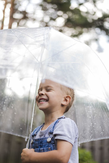 Happy boy holding umbrella while standing outdoors during rainy season