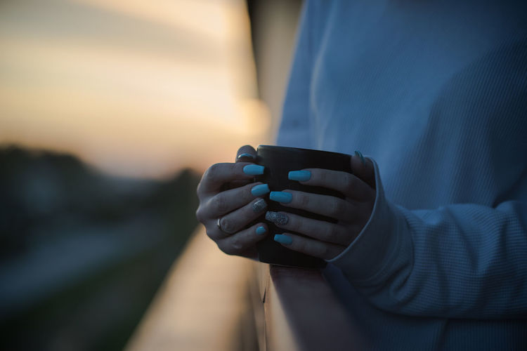 Midsection of woman holding coffee cup in balcony during sunset