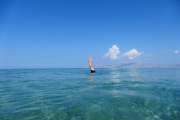 Rear view of man swimming in sea against sky with handstand