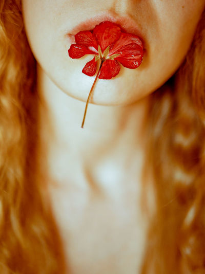 High angle view of young woman holding a red flower with her lips. blond hair, red head. 