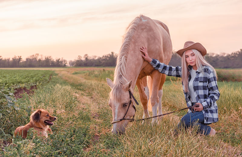 Teenage girl with horse kneeling on land during sunset