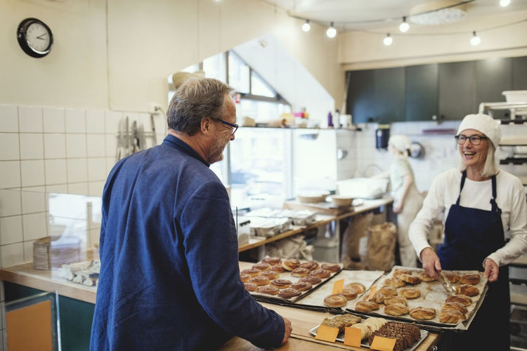 Smiling female owner showing fresh baked food to customer at bakery