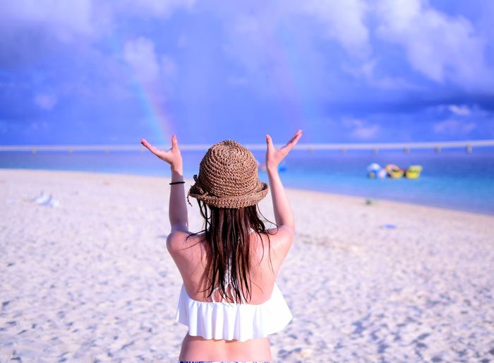 Rear view of woman gesturing while standing at beach against sky