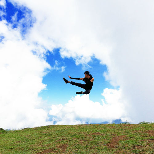 Man jumping on field against sky