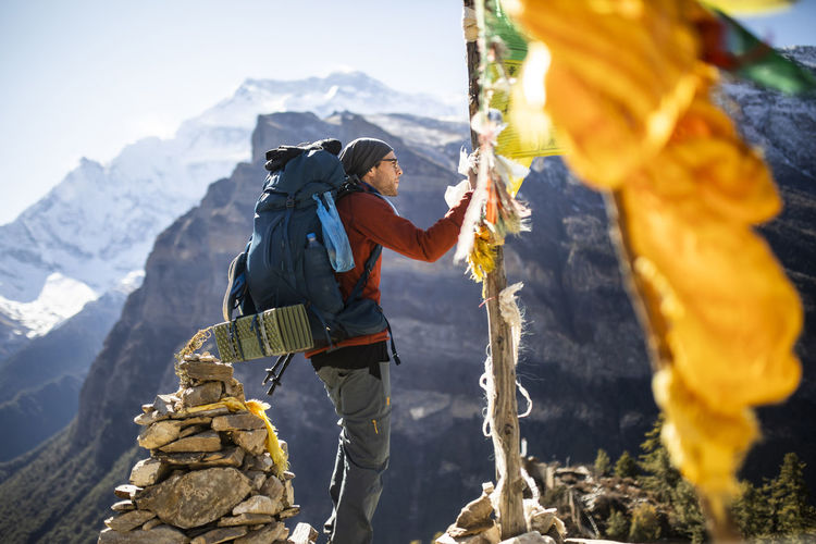Side view of male hiker hanging buddhist prayer flag on rope during trekking in himalayas mountains in nepal