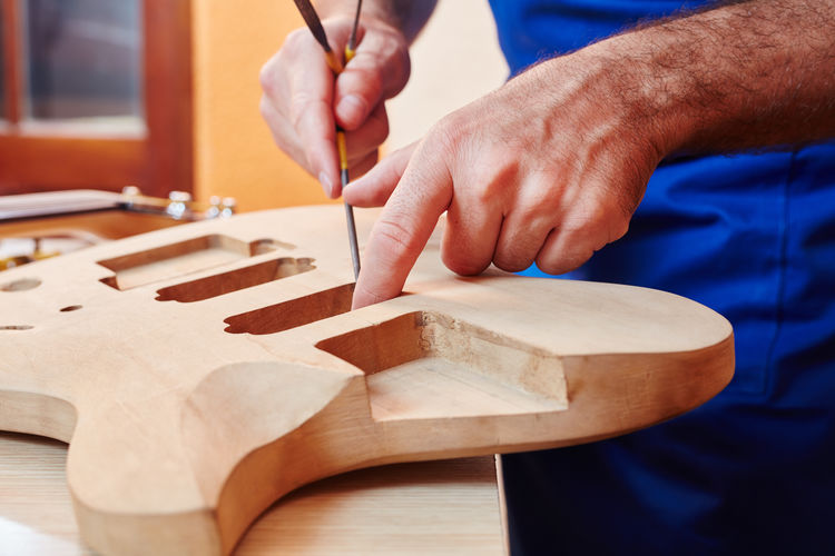 Midsection of worker making guitar at workshop