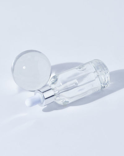 Glass bottle with natural hyaluronic acid for skin care treatment placed near glass ball on white background in light room