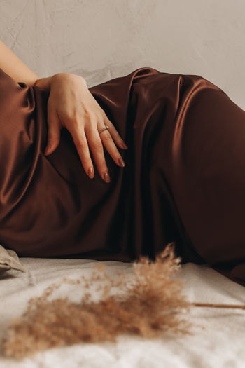 Female body in silk brown dress. close up female hand with a ring and autumn beige dry plant