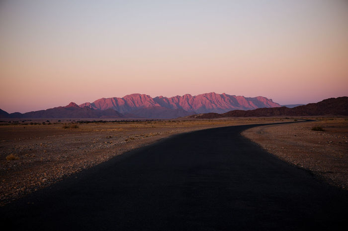 Empty road and mountains against clear sky during sunset