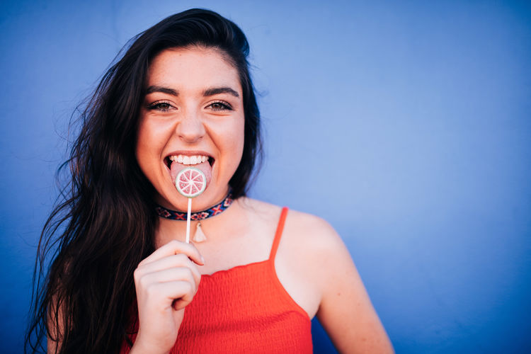 Portrait of young woman eating candy while standing against wall