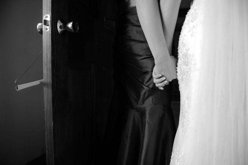 Midsection of bride and friend holding hands at doorway