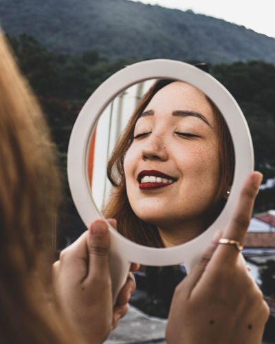 Close-up portrait of a smiling young woman reflected on a small mirror.