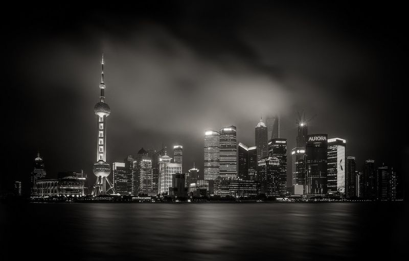 Low angle view of illuminated oriental pearl tower amidst buildings in front of river at night