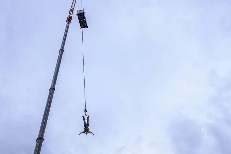 Low angle view of man bungee jumping from crane against sky