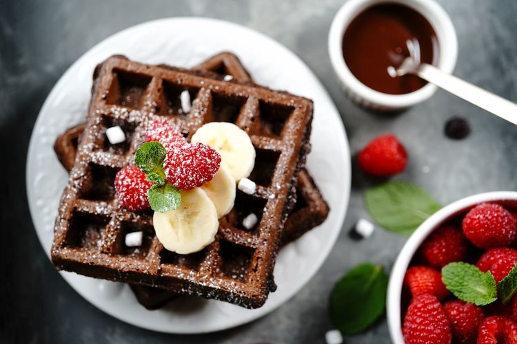 Chocolate waffles topped with berries bananana served with chocolate sauce