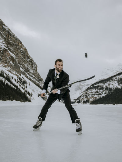 Man in suit and ice skates juggles hockey puck on frozen lake louise