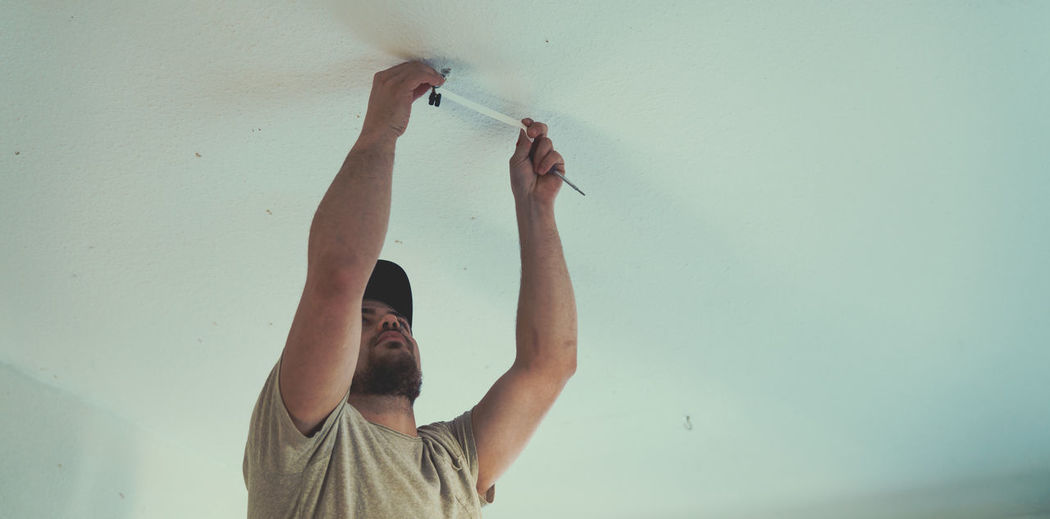 Low angle view of man repairing ceiling at home