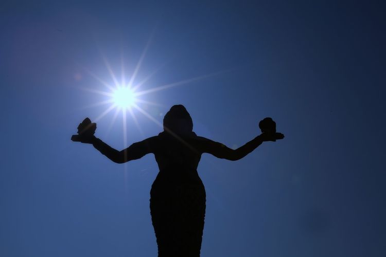 Rear view of silhouette woman standing against blue sky