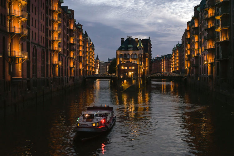 Boats in canal amidst buildings in city at dusk