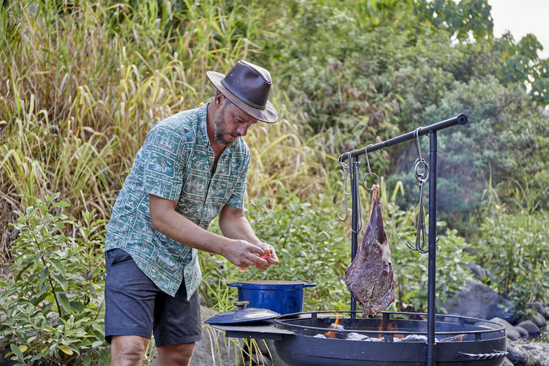Chef cooking over open flame at campsite along streambed