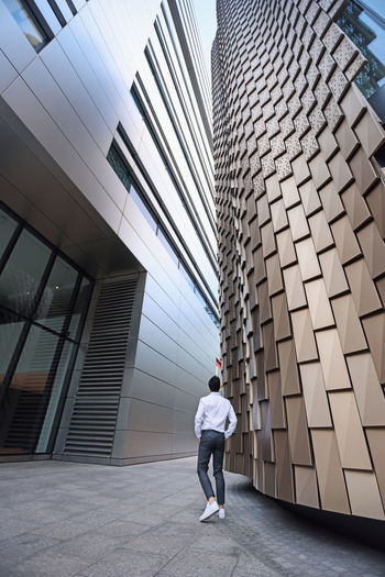 Rear view of man walking by modern building in city