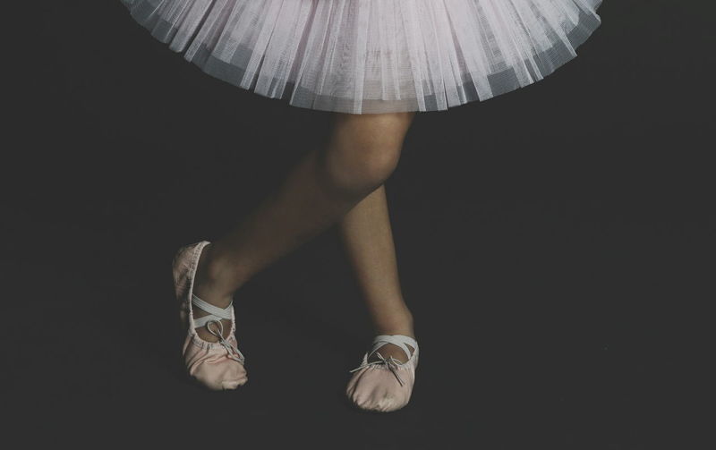 Low section of ballerina standing against black background