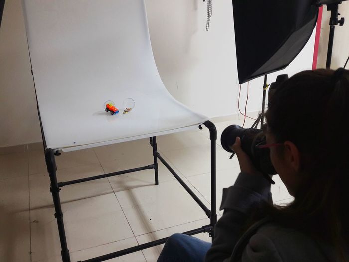 High angle view of young woman photographing toys on chair in studio
