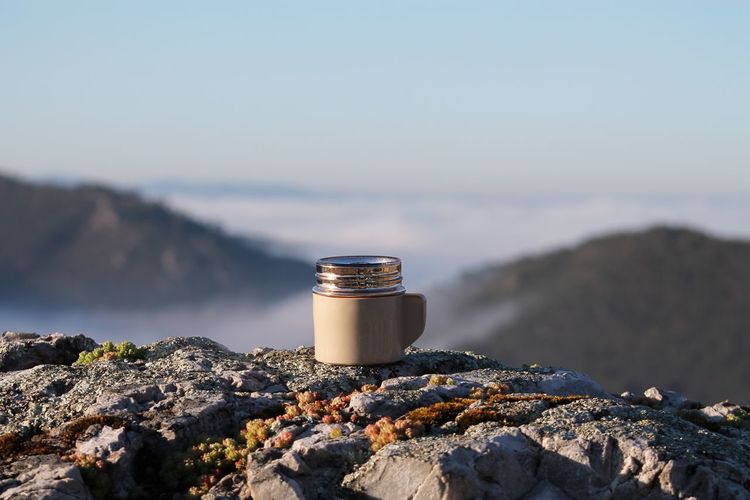 Abandoned lid of insulated drink container on rock against sky