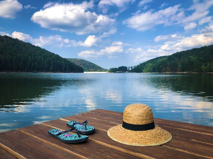 Straw hat and flip flops on wooden pontoon near the lake