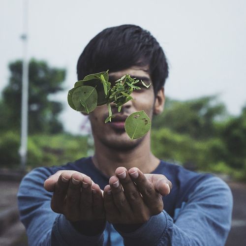 Close-up portrait of man holding leaves against sky