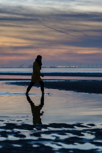 Side view of man wading in sea against sky during sunset