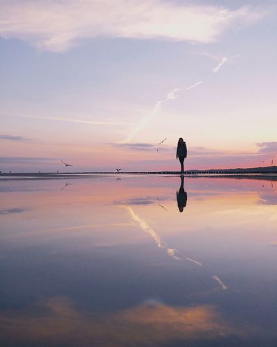 Young woman reflecting on beach against sky during sunset