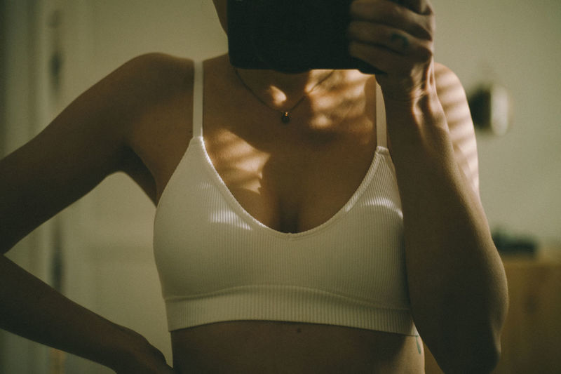 Midsection of woman in the bra in the mirror, standing at home