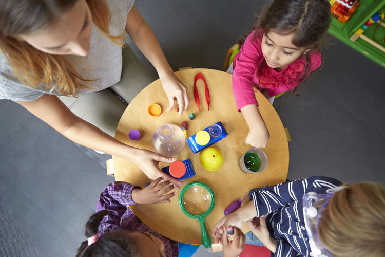 Overhead view of teacher assisting children in science experiment at preschool