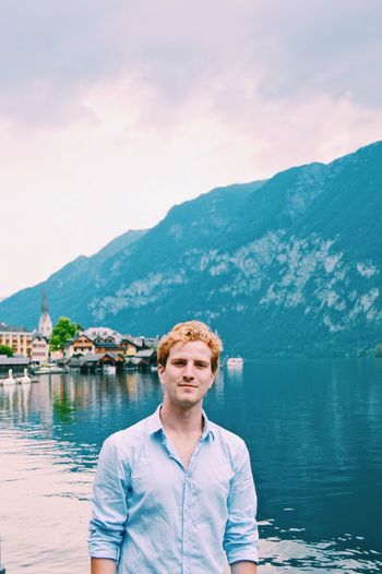 Portrait of young man standing by lake against mountain