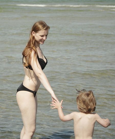 Woman in bikini holding son hand at sea shore