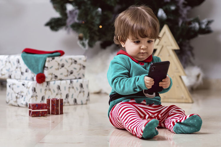 Boy holding mobile phone while sitting on floor