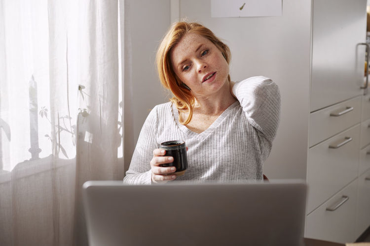 Woman holding her neck while using laptop