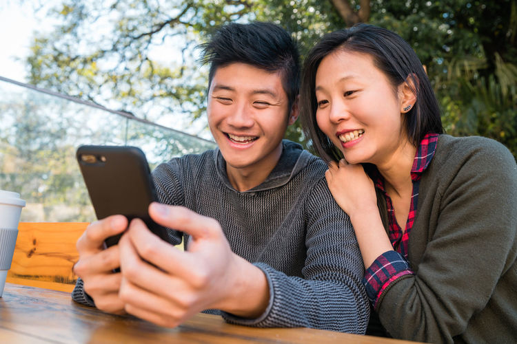 Smiling couple using phone sitting on bench at park