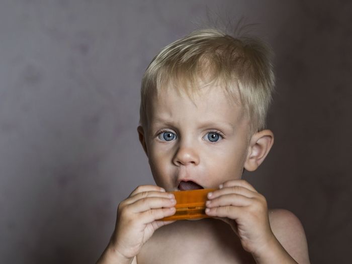 Portrait of shirtless boy playing harmonica against wall