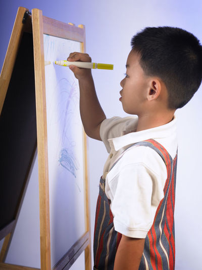 Close-up of boy holding camera standing against wall