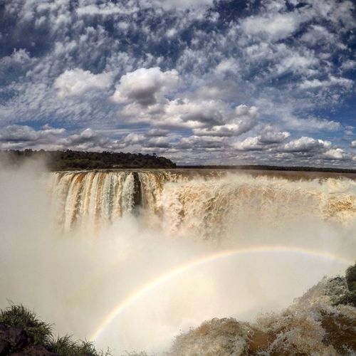Waterfall and rainbow against cloudy sky
