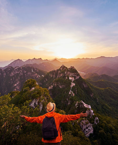 Rear view of man standing on mountain against sky during sunset
