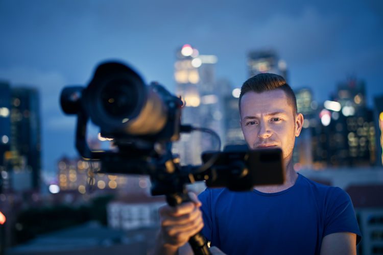 Man filming with camera and gimbal. portrait of videographer against urban skyline at night.
