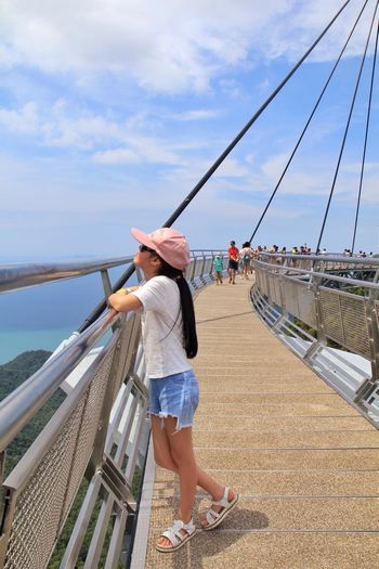 Side view of girl standing on footbridge against sky