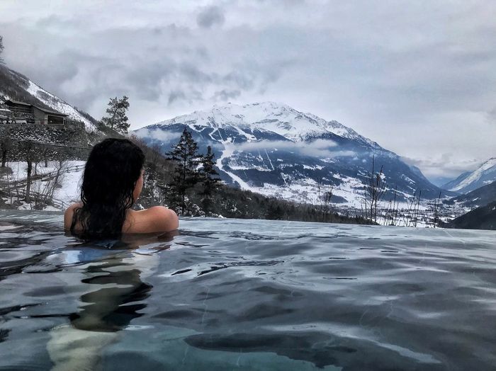 Rear view of woman swimming in infinity pool against snowcapped mountains