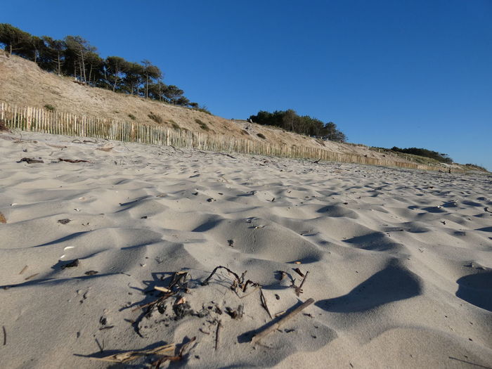 Footprints on sand at beach against clear blue sky