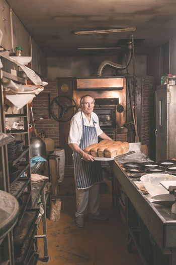 Full length portrait of baker holding breads in tray at bakery