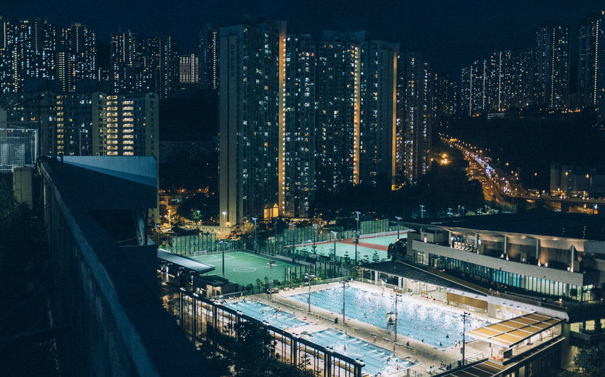 Illuminated country club against modern buildings in city at night