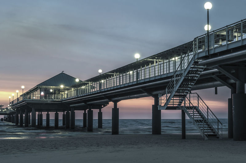 Low angle view of illuminated pier over sea at sunset